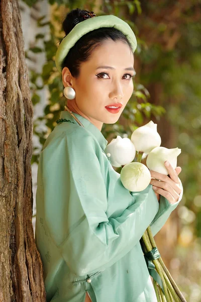 身穿浅绿色传统服装 手持白莲花 看着相机的年轻漂亮越南女子的画像 — 图库照片