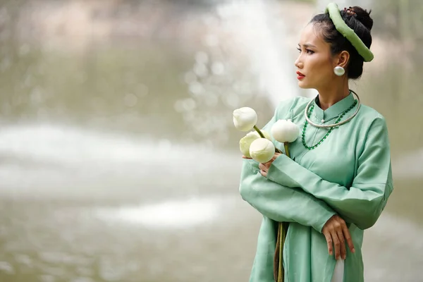 手にハスの花と水を見て川に立って伝統的な衣装で心配豪華な若いベトナム人女性 — ストック写真