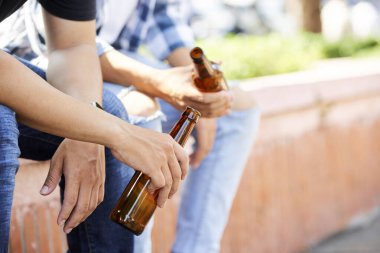 Açık havada otururken ellerinde bira şişeleri olan genç erkeklerin yakın çekimi.