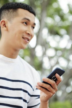 Asyalı genç adam dışarıda yürürken cep telefonunu kullanıyor.