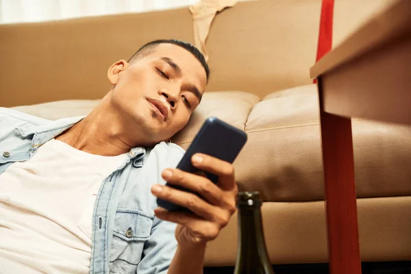 Sklíčený Asijský Muž Sedí Podlaze Opírá Pohovku Kontroluje Sociální Média — Stock fotografie