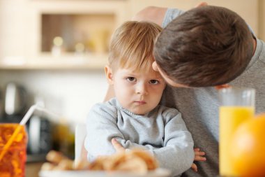 Babasının dizlerinin üzerinde otururken kameraya bakan küçük şirin bir çocuğun portresi.
