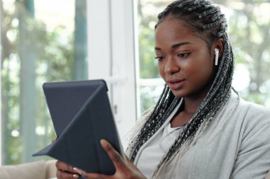 Portrait of pretty young Black woman with braided hair wearing earbuds and video calling her friend of family member clipart