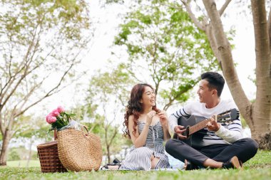 Yakışıklı Vietnamlı genç bir adam parkta piknik yaparken kız arkadaşına gitar çalıp şarkı söylüyor.