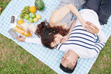 Mutlu, genç Vietnamlı çift parkta battaniyenin üzerinde dinleniyor suşi ve meyve yedikten sonra birbirlerine bakıyor, yukarıdan bakıyorlar.