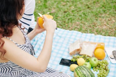 Genç bir kadının erkek arkadaşıyla romantik piknik yaparken keskin bir bıçakla portakal soyarkenki görüntüsü.