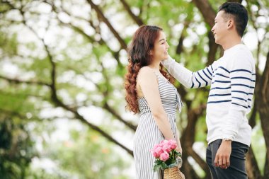 Parkta dururken gülümseyen güzel kız arkadaşının yüzüne dokunan mutlu Asyalı genç adam.