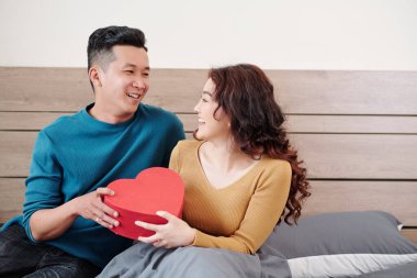 Mutlu genç Vietnamlı adam gülümseyen güzel kız arkadaşına Sevgililer Günü hediyesi veriyor.