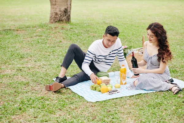 一对年轻的越南夫妇坐在公园的毛毯上 从篮子里拿出酒和食物 — 图库照片