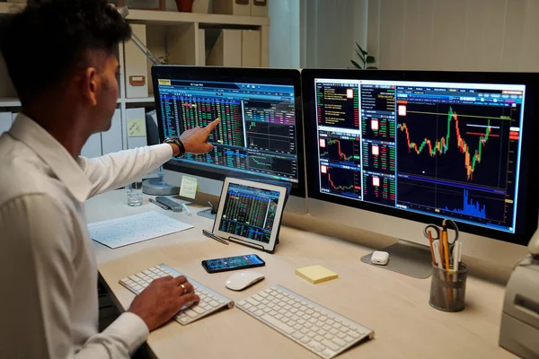 专业的印度年轻交易员在黑暗的办公室工作 指着电脑屏幕上的股票市场信息 — 图库照片