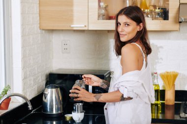 Güzel genç bir kadın mutfak tezgahında Vietnam tarzı kahve yapıyor ve kameraya gülümsüyor.