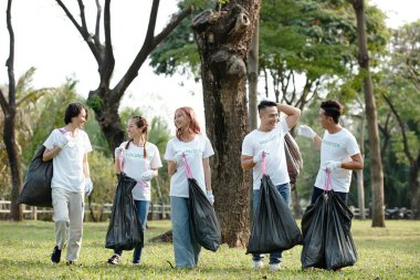 Park temizlenirken ve çöpleri toplarken ellerinde plastik poşetler tutan neşeli gönüllüler.