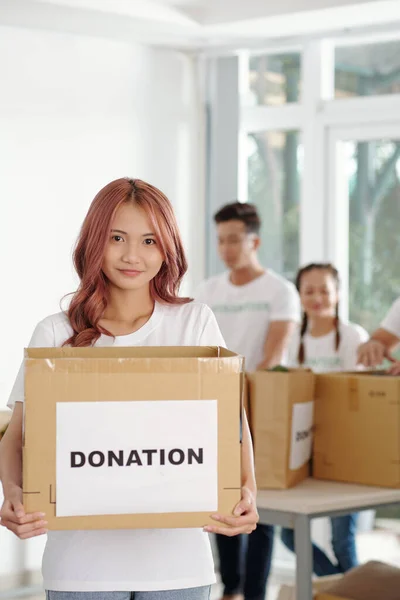 ピンク色の髪をした若いアジアの女性は 慈善財団に寄付された食料品や服の大きな箱を持っています — ストック写真