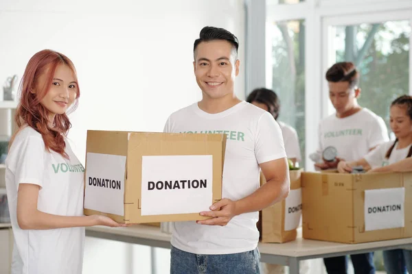 Young Asian couple working as volunteers in donation center, they packing boxes for people in need