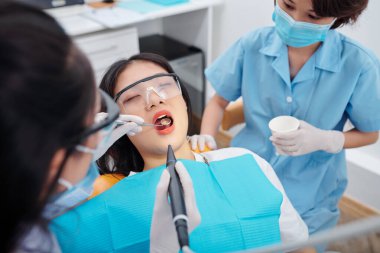 Diş ağrısı çeken genç bir bayanın dişlerini delen bir diş hekimi.