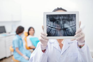 Dişçi ekranda kadın hastanın çene röntgeni ile tablet bilgisayarı gösteriyor