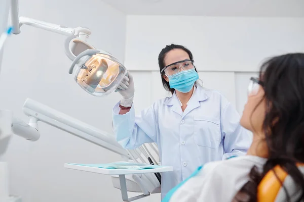 Erfahrene Zahnärztin Mit Schutzbrille Und Medizinischer Maske Schaltet Lampe Ein — Stockfoto