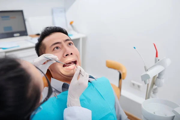 在诊所接受牙齿治疗时吓得满脸笑脸的年轻亚洲男子 — 图库照片