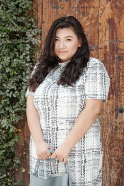 Genç, çekici, iri yarı bir kadının portresi. Elinde deri bir çantayla dışarıda duruyor ve kameraya bakıyor.