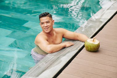 Neşeli orta yaşlı adam spa otelinin havuzunda duruyor ve lezzetli hindistan cevizi kokteyli içiyor.