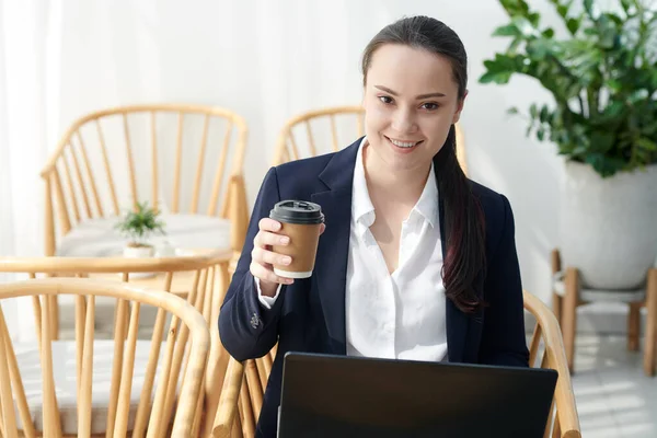 Confident pretty young woman with cup of coffee running her online business