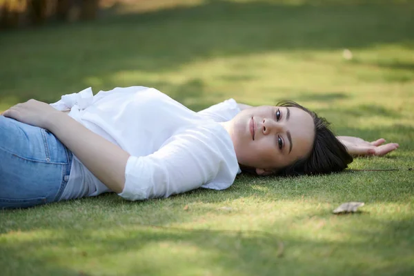 美丽的微笑的年轻女子躺在公园的地面上 看着相机 — 图库照片