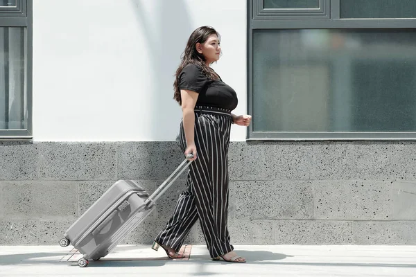 プラスサイズの若い女性は 鉄道駅へのスーツケースと通りを歩く — ストック写真