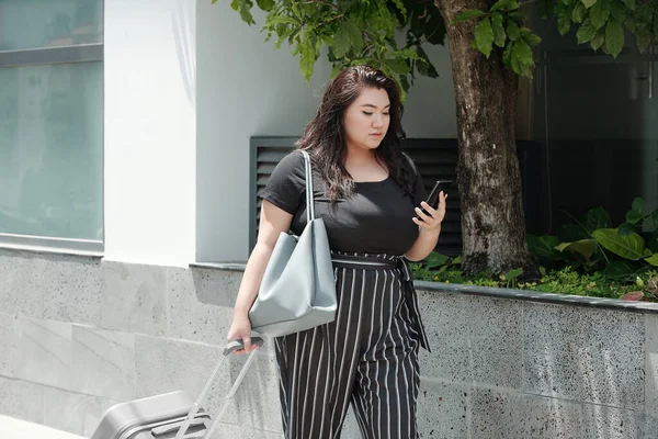 漂亮而严肃的女人 背着行李在街上走来走去 用智能手机查看短信 — 图库照片