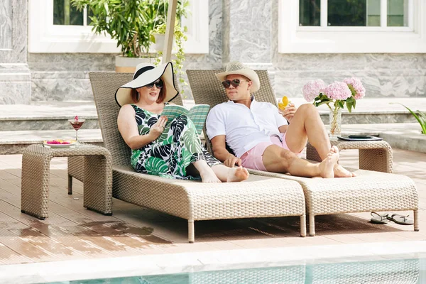 Mature Couple Reading Drinking Cocktails Relaxing Chaise Lounges Swimming Pool — Stock Photo, Image