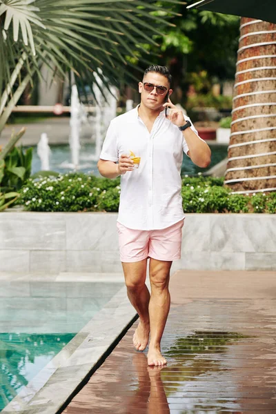 Bir Bardak Burbonlu Yakışıklı Adam Havuz Kenarında Yürüyor Ortağıyla Telefonda — Stok fotoğraf
