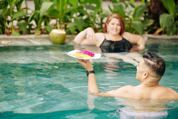 Hombre Llevando Plato Con Rebanadas Fruta Esposa Refrescante Piscina Vista — Foto de Stock