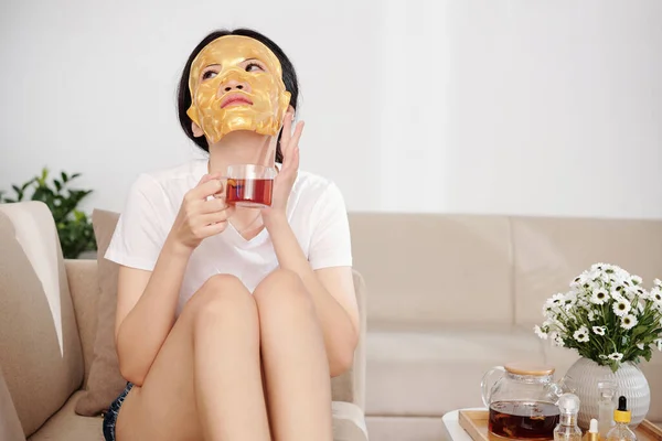 Junge Frau Mit Feuchtigkeitsspendender Lakenmaske Auf Dem Gesicht Trinkt Eine — Stockfoto