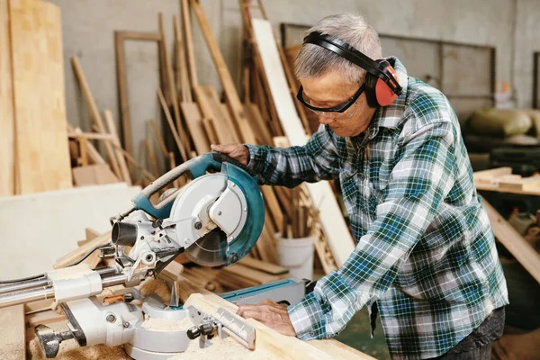 真剣なシニアアジア人男でEarmuff切断木板とともに円形見でワークショップ — ストック写真