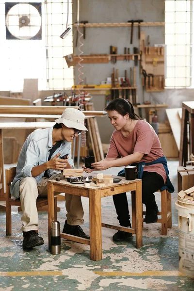 Young Asian carpenters having coffee break and discussing reference picture that customer sent via social media