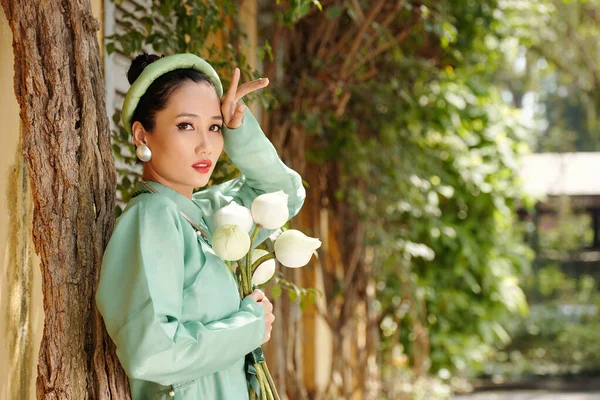 严肃的越南妇女手持一束荷花站在树旁看着相机的画像 — 图库照片