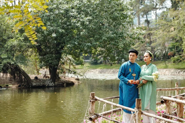 身穿传统服装的新婚夫妇站在城市公园的池塘边 看着水 — 图库照片