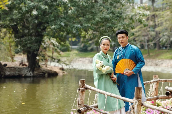 穿着传统服装和头饰的年轻貌美的越南夫妇看着城市池塘里的水 — 图库照片