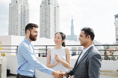 Gülümseyen proje yöneticisi ve yatırımcı çatıda buluştuktan sonra el sıkışıyor