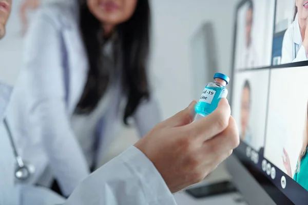 オンライン会議で彼の同僚にコロナウイルスに対する新しいワクチンでバイアルを示す医師の手 — ストック写真