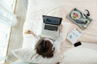 İş kadını kahvaltıda taze meyve yerken bilgisayarındaki satış raporlarını analiz edip yatak konsepti üzerinde çalışıyor.