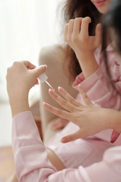 当朋友在她手上吹干指甲油时 年轻女人在她的指甲上涂透明的底漆 — 图库照片