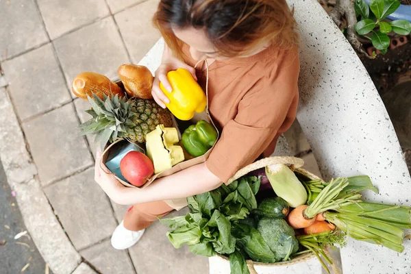 漂亮的年轻女子拿着两袋新鲜蔬菜 水果和面包坐在长椅上 — 图库照片