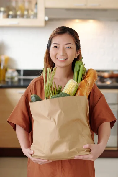 台所に立つと新鮮な野菜の紙のパッケージを保持幸せな若い女性の肖像画 — ストック写真