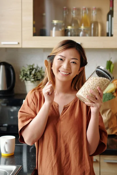站在厨房里拿着一罐燕麦和木勺的快乐而兴奋的年轻女子的画像 — 图库照片