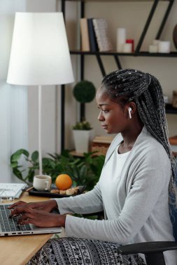 Ciddi bir iş kadını oturma odasında dizüstü bilgisayarla çalışırken kulaklık takıyor.