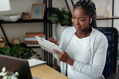 Gülümseyen güzel kadın dizüstü bilgisayarda webinar izleyip not alıyor, önemli detaylar yazıyor.