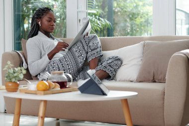 Coronavirüs salgını nedeniyle evden çalışan bir kadın kanepede oturup önemli belgeler veya sözleşmeler okuyor.