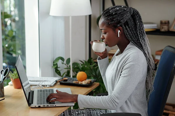 年轻的女商人喝着茶或咖啡 在笔记本电脑屏幕上阅读电子邮件 — 图库照片