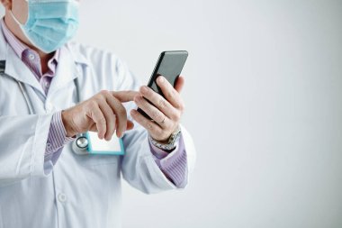 Maskeli ve beyaz önlüklü tanımlanamayan doktorun yakın plan görüntüsü. Telefondaki mesaj gri arka planda.
