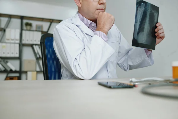 白衣を着た放射線技師がテーブルに座り X線画像をオフィスで分析しながら診断を考える — ストック写真